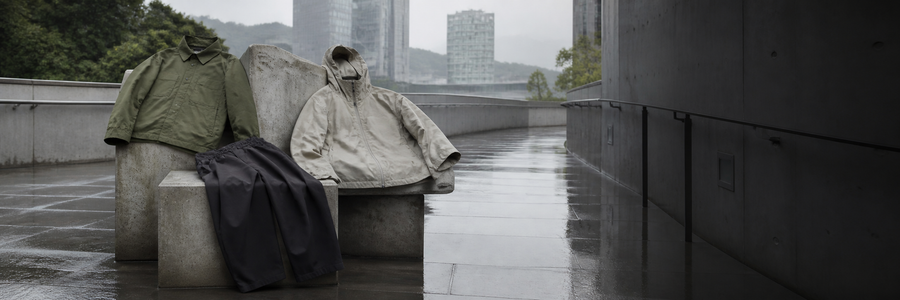 雨上がりの都市空間にオリーブのオーバーシャツ、チャコールのワイドパンツ、ストーンのフードジャケットを配したSTILL TERRAINのブランドビジュアル